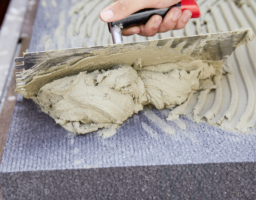 Gleichmäßiges Auftragen des Klebers mittels Zahnspachtel sorgt dafür, dass die Dämmplatte fest und ohne Hohlräume an der Außenwand sitzt.