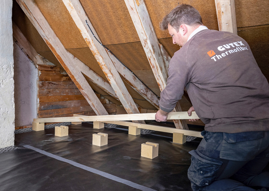 Ein Handwerker baut die Unterkonstruktion für eine begehbare Dämmung der obersten Geschossdecke auf.