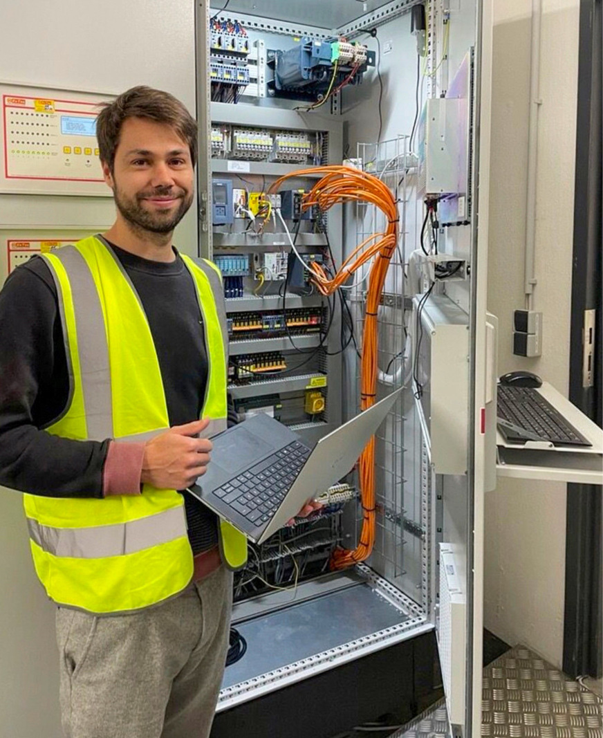 Flexality-Mitarbeiter Justus Hinken steht vor einem Schaltschrank, in dem die Daten aus dem Betrieb der Anlage stecken.