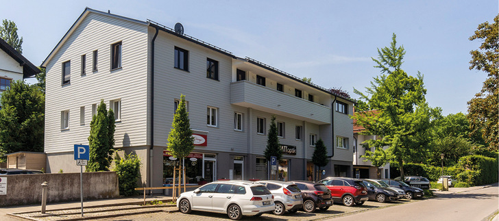 Die Fassaden des aufgestockten Wohn- und Geschäftshauses in Schondorf sind mit einer Stülpschalung aus Faserzement (Hardie Plank) bekleidet – diese ist zwar etwas teurer als eine Holzfassade, spart aber dafür jährlich so viel an Wartungskosten ein, dass sich die Mehrkosten rasch amortisiert haben.