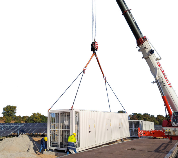 Ein Batteriespeicher wird durch einen Schwerlastkran auf das Fundament gehoben.