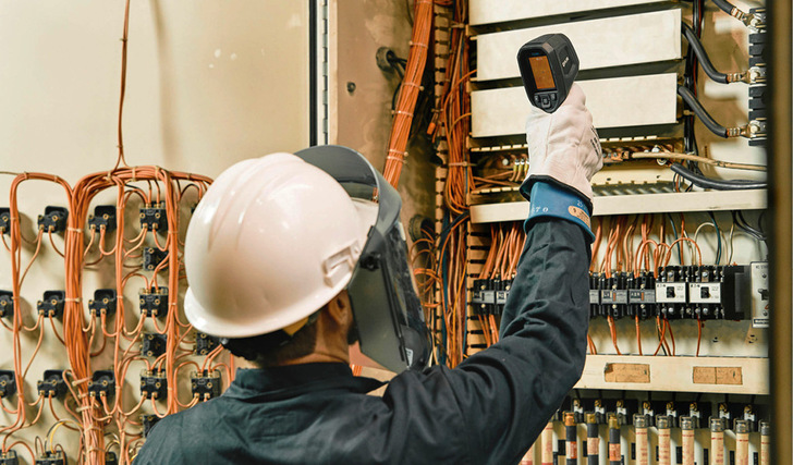 Elektriker in Sicherheitsausrüstung überprüft mit einer Wärmebildkamera Schalttafeln und Leitungen. - © Bild: Flir