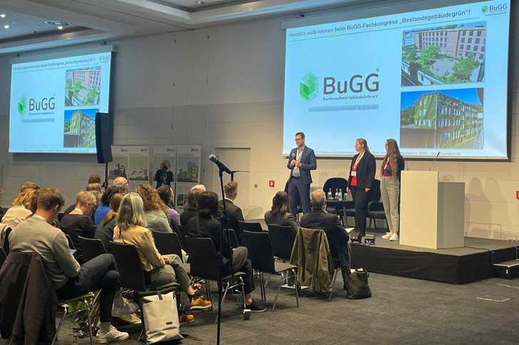 BuGG-Präsident Gunter Mann begrüßt die Teilnehmenden auf der Bühne mit Sylvia van Meegen, Assistentin und Michelle Bruchmüller, Veranstaltungsmanagerin (rechts außen).
