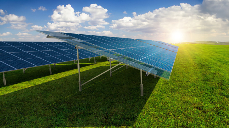 Reihen von Solarmodulen auf einer grünen Wiese unter blauem Himmel mit vereinzelten Wolken und hellem Sonnenlicht. - © K2 Systems