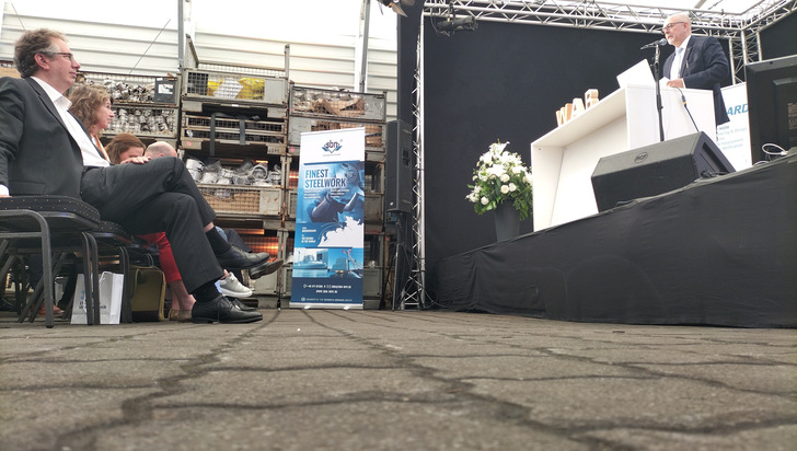 Windforce 2025 in Bremerhaven: Jens Assheuer, Vorstandsvorsitzender WAB, Hester Somsen, Botschafterin der Niederlande in Deutschland im Publikum, auf der Bühne spricht der Staatsrat bei der Senatorin für Wirtschaft, Häfen und Transformation in Bremen, Kai Stührenberg.