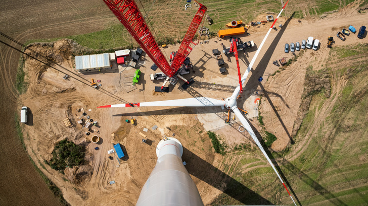 Luftaufnahme einer im Bau befindlichen Windkraftanlage mit Kränen, Fahrzeugen und Arbeitern vor Ort. - © Tarnero - stock.adobe.com