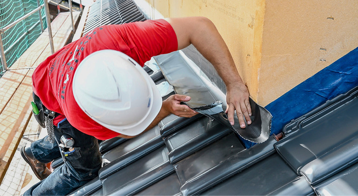 Ein Dachhandwerker heftet das Anschlussband Ubiflex Finio an die Holzfaserdämmung der Gaube.