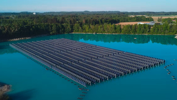 Schwimmende Solarmodule, die in Reihen auf einem ruhigen blauen See angeordnet sind, umgeben von Bäumen und weit entfernten Feldern. - © Foto: SINNPOWER