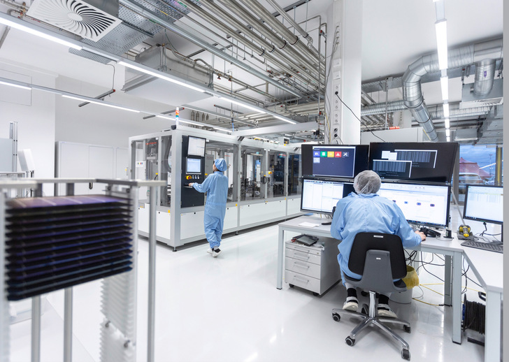 Zwei Personen in Reinraumanzügen arbeiten an Computern und Maschinen in einem Hightech-Labor. - © Foto: Dirk Mahler - Fraunhofer ISE