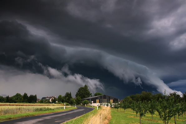 Dunkle Gewitterwolken drohen über einer ländlichen Landschaft mit einer Straße, Feldern und verstreuten Häusern. - © Adrian72 - stock.adobe.com