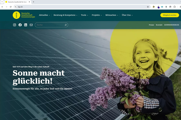 Mädchen hält Blumen, lächelt, hinter ihr Solarzellen, gelbe Sonnenblende in der Ecke. Text: „Sonne macht glücklich!“. - © DGS
