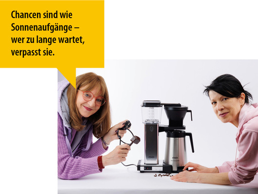 Zwei Frauen bereiten lächelnd Kaffee mit einer Filterkaffeemaschine zu. In einer gelben Sprechblase steht ein deutsches Zitat über Chancen. - © Bild: Sabine Gärtner