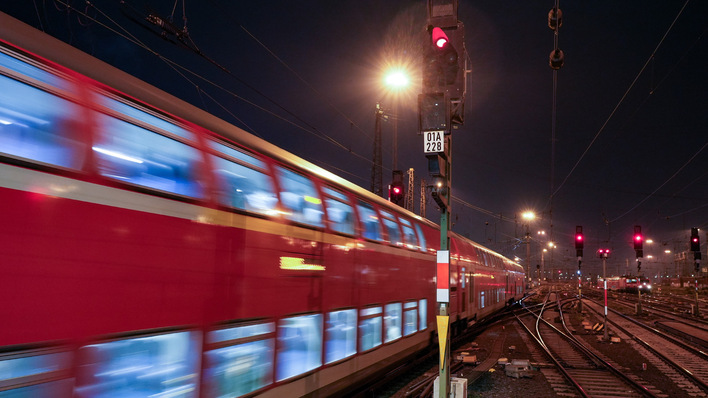 Ein roter Zug fährt nachts schnell an einem roten Signallicht auf Gleisen vorbei. - © Deutsche Bahn AG / Volker Emersleben