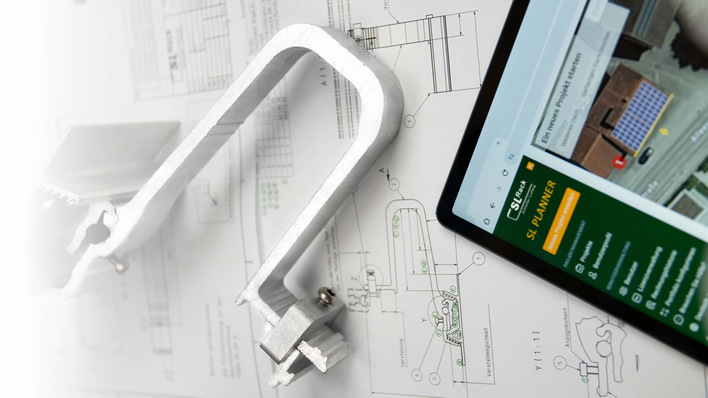 Auf einer weißen Fläche liegen eine Metallklammer, technische Zeichnungen und ein Tablet mit einer Site-Planer-App. - © SL Rack