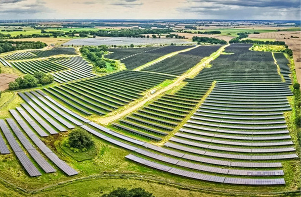 Luftaufnahme einer großen Solarzellenfarm in einer ländlichen Landschaft mit grünen Feldern und bewölktem Himmel. - © Foto: Vattenfall
